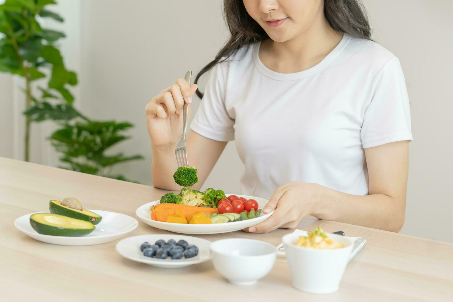 Dieting, diet asian young woman, girl eating, holding fork at broccoli, diet plan nutrition with fresh vegetables salad, enjoy meal on table at home. Nutritionist of healthy, nutrition of weight loss. photo