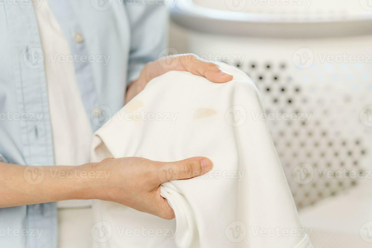 Housewife, asian young woman hand in holding shirt, showing making stain, spot dirty or smudge on clothes, dirt stains for cleaning before washing, making household working at home. Laundry and maid. photo