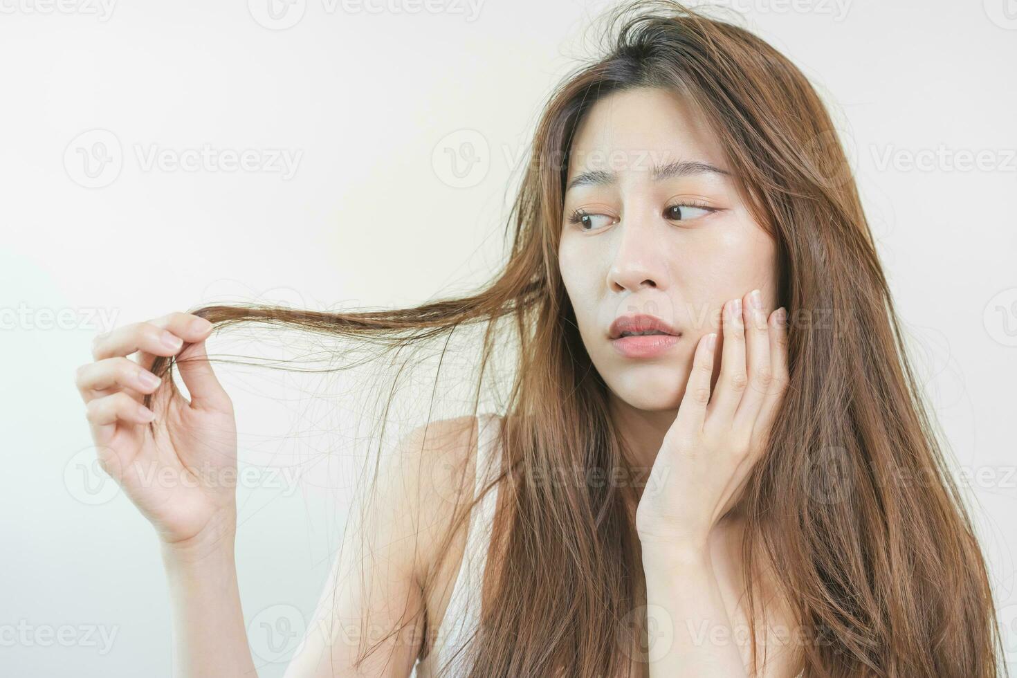 Damaged Hair, frustrated asian young woman, girl hand in holding splitting ends, messy unbrushed dry hair with face shock, long disheveled hair, health care of beauty. Portrait isolated on background. photo