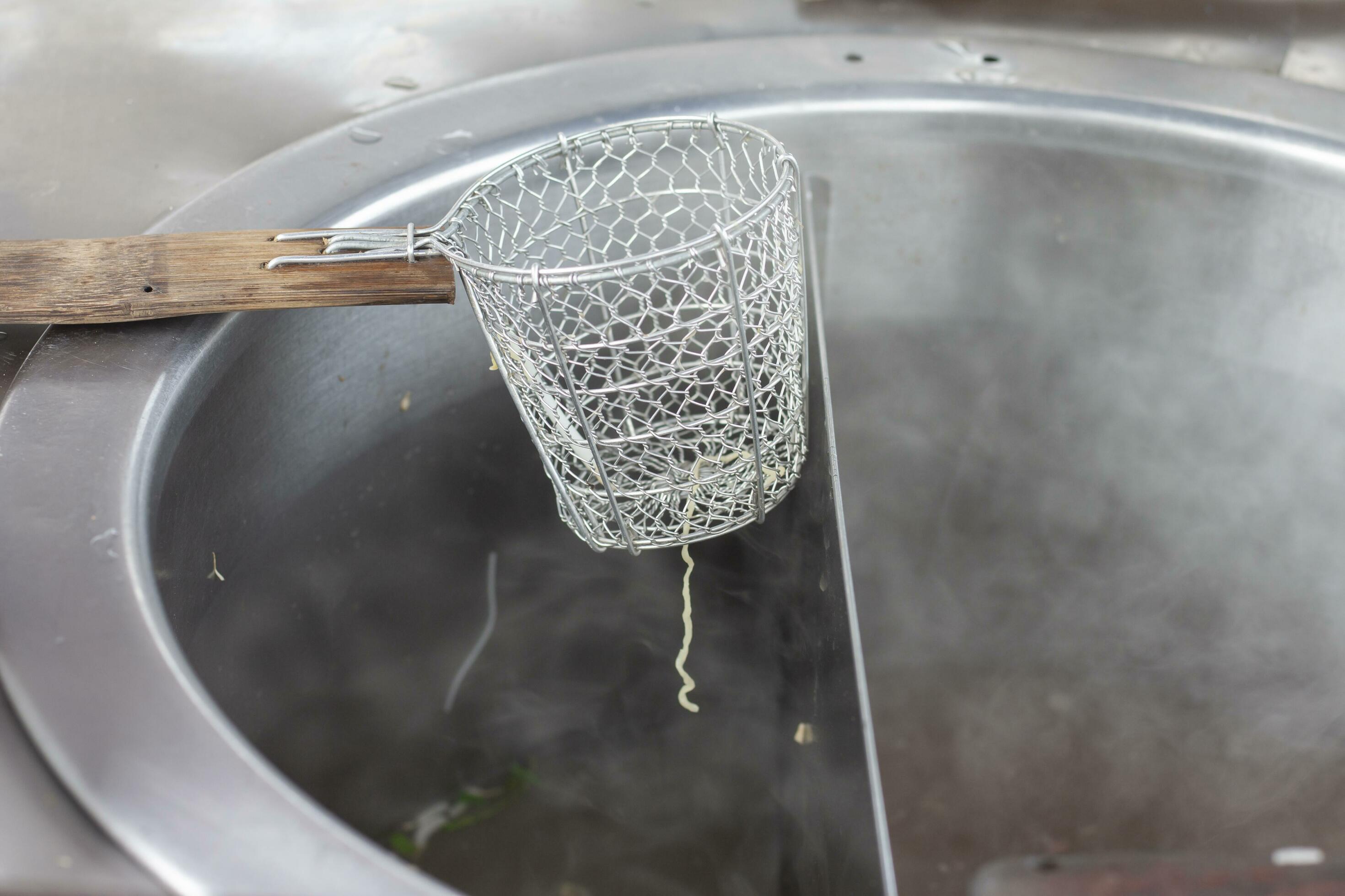 Strainer basket for blanching noodles laying over a pot covered with