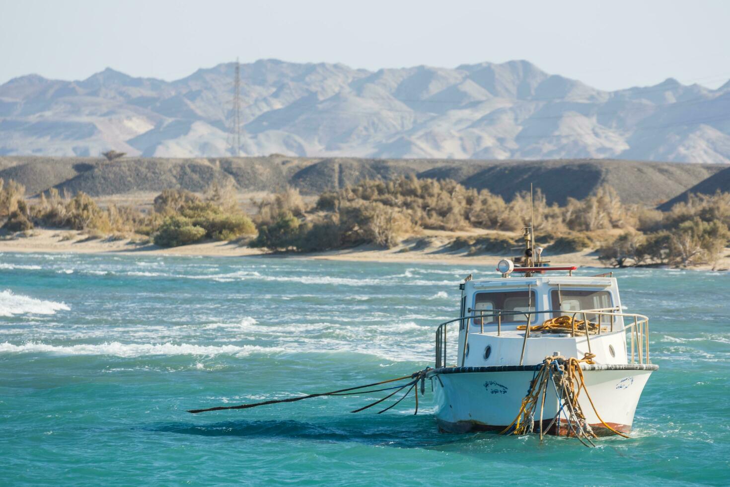 white boat with many ropes in the sea with mountains from the desert in egypt photo