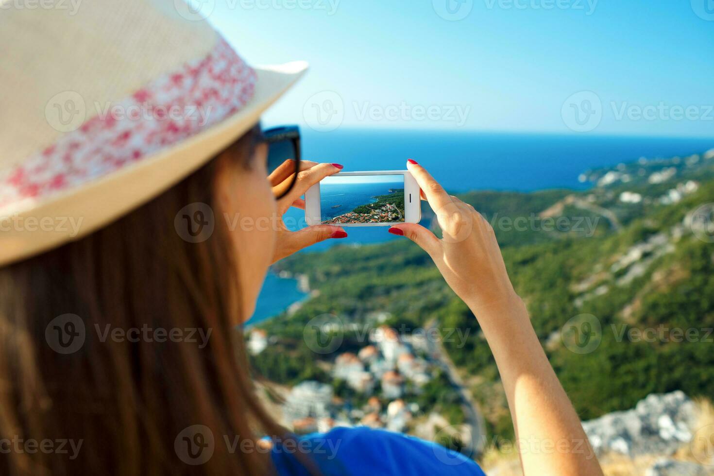 Girl in hat making photos of the Adriatic sea by the smartphone