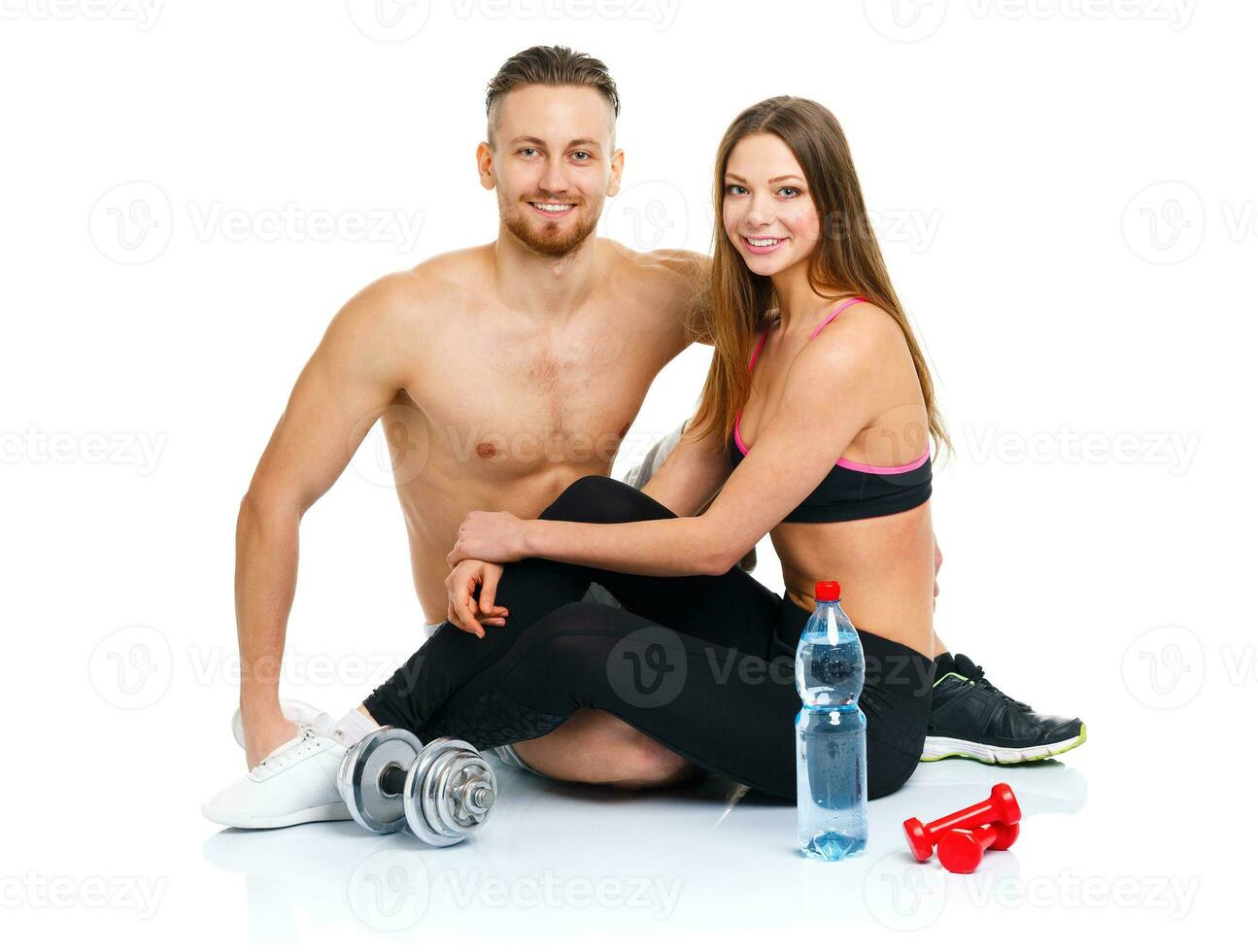Sport couple - man and woman after fitness exercise with dumbbells and bottle of water sitting on the white photo