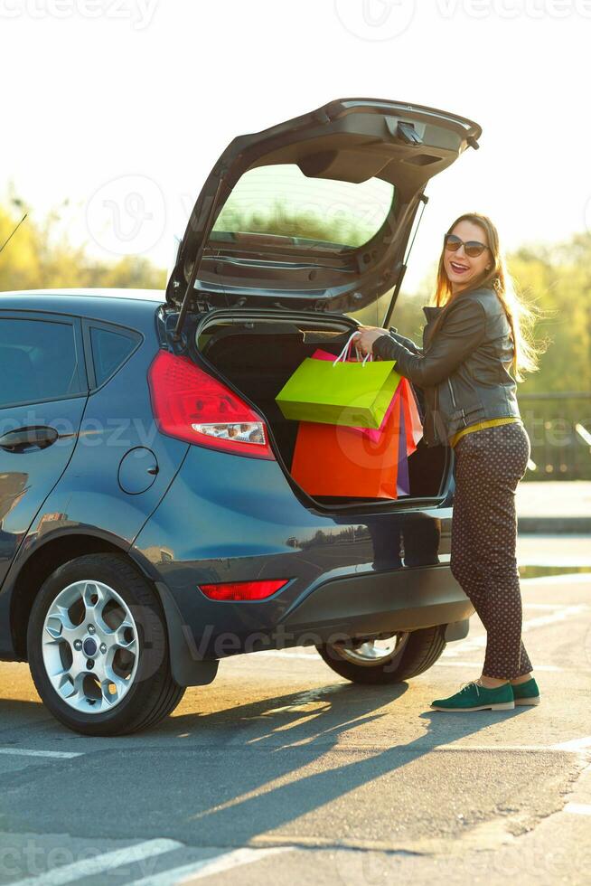 caucásico mujer poniendo su compras pantalones dentro el coche maletero foto