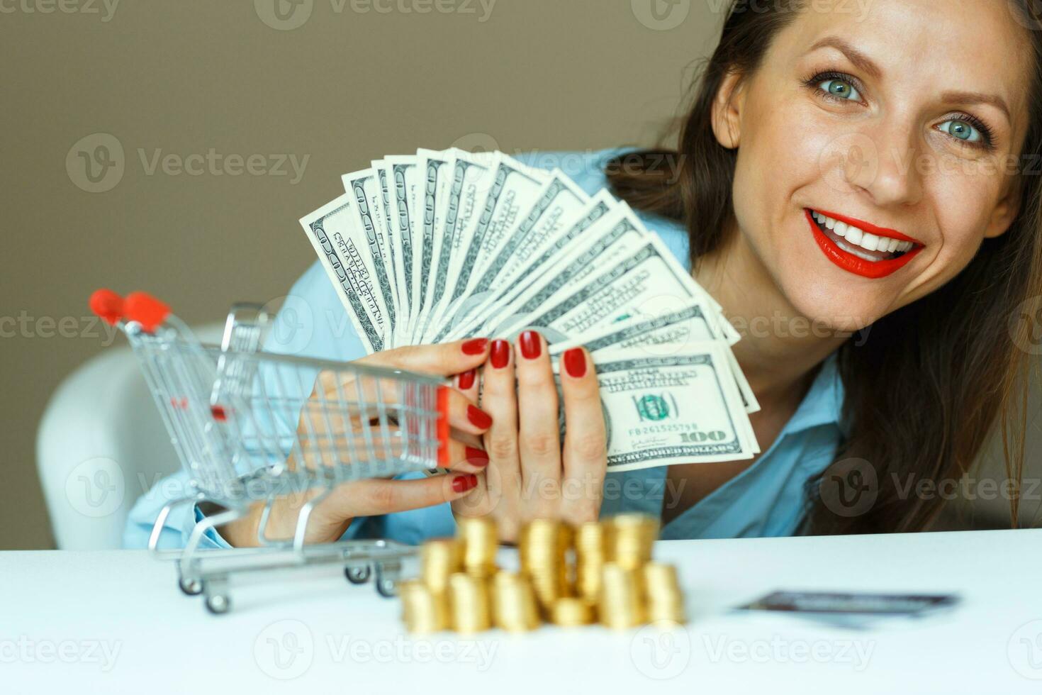 joven sonriente mujer participación dinero en efectivo, y en el mesa son monedas, crédito tarjeta y el compras carro foto