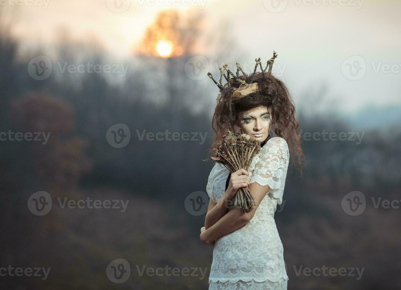 joven niña en un blanco cordón vestido, un corona de leña menuda con un ramo de flores de seco flores foto