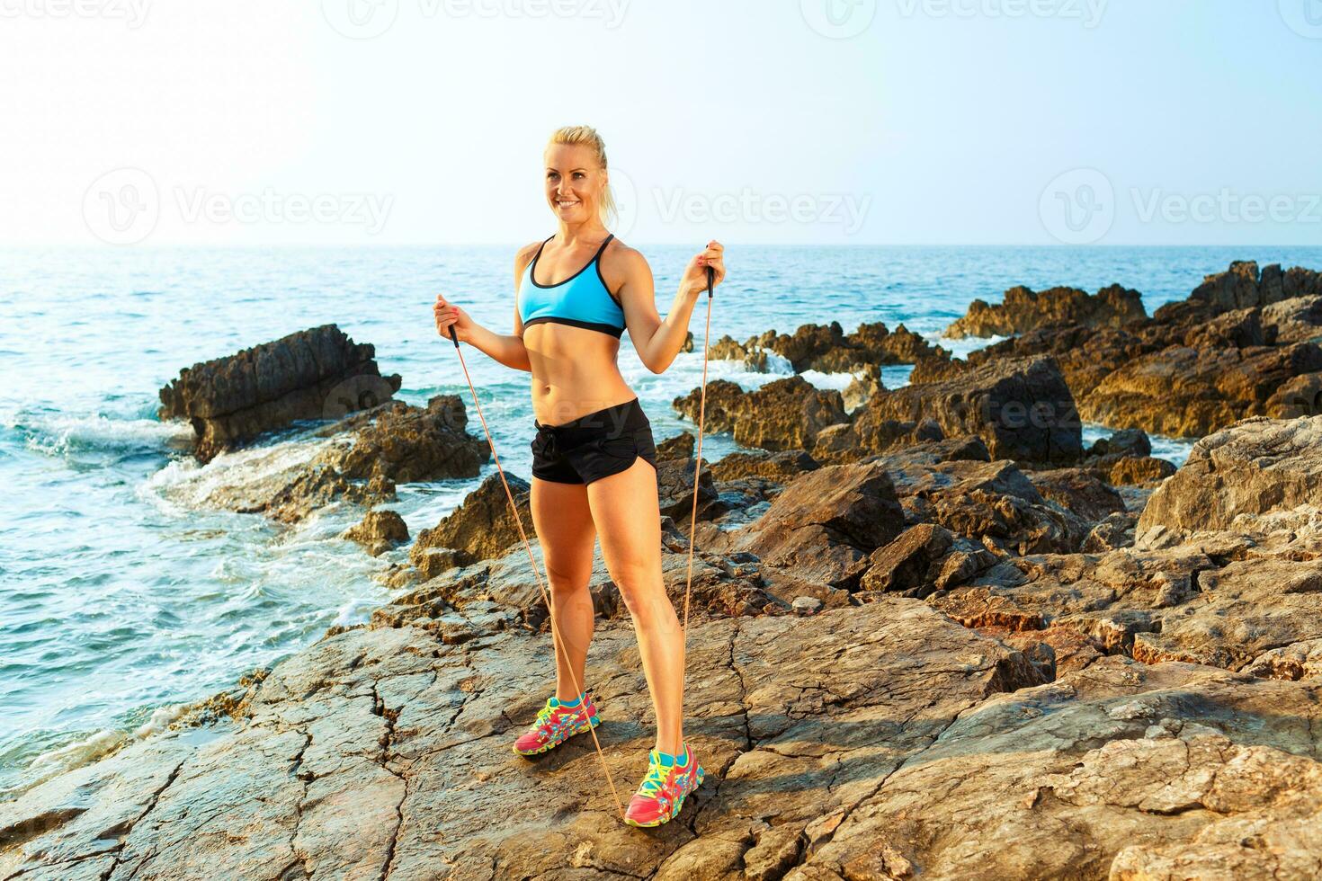 Athlete woman doing sport exercising with the rope on the rocks by the sea photo