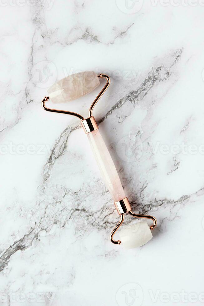 Pink jade roller massager for face on white marble. photo