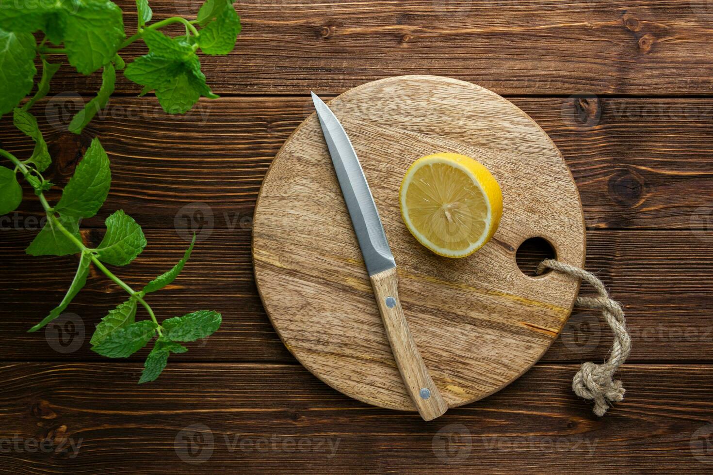 Lemon with knife on cutting board on wooden background. photo