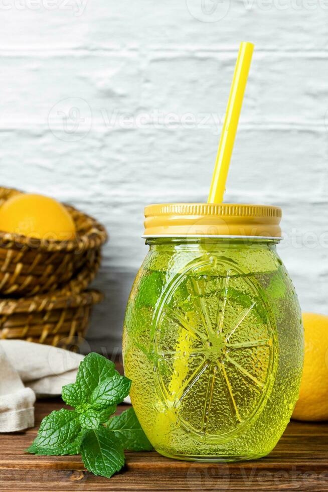 Water with mint in yellow glass, lemon in basket on wooden table. photo