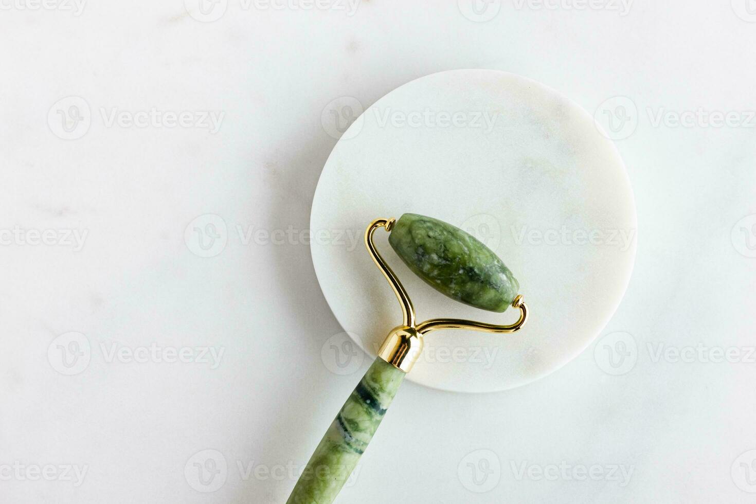 Green jade roller massager for face on white marble. photo