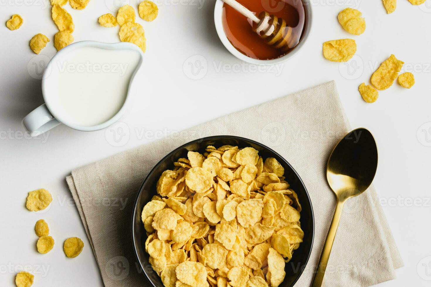 Corn flakes in dark bowl with milk and honey on white background. photo