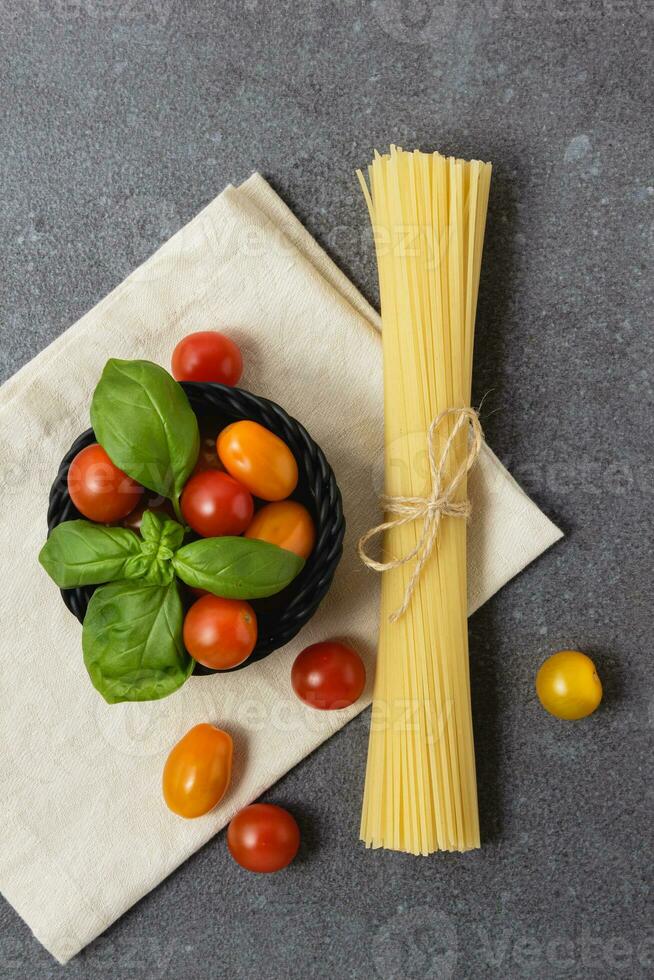 Raw pasta spaghetti with cherry tomatoes in basket on concrete background. photo