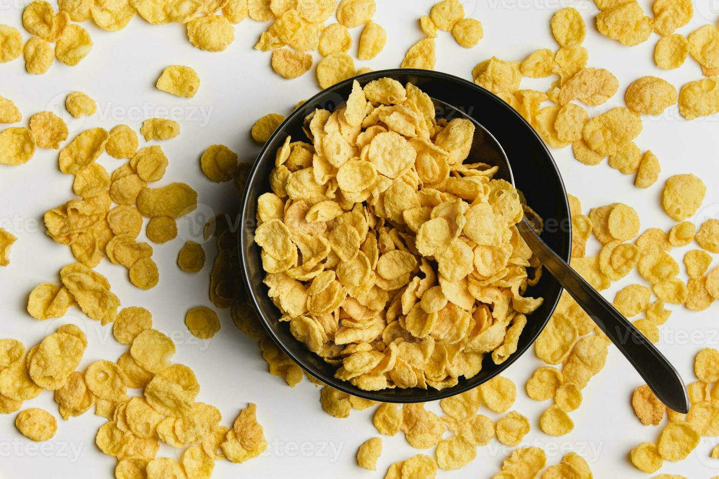 Corn flakes in dark bowl with spoon on white background. photo
