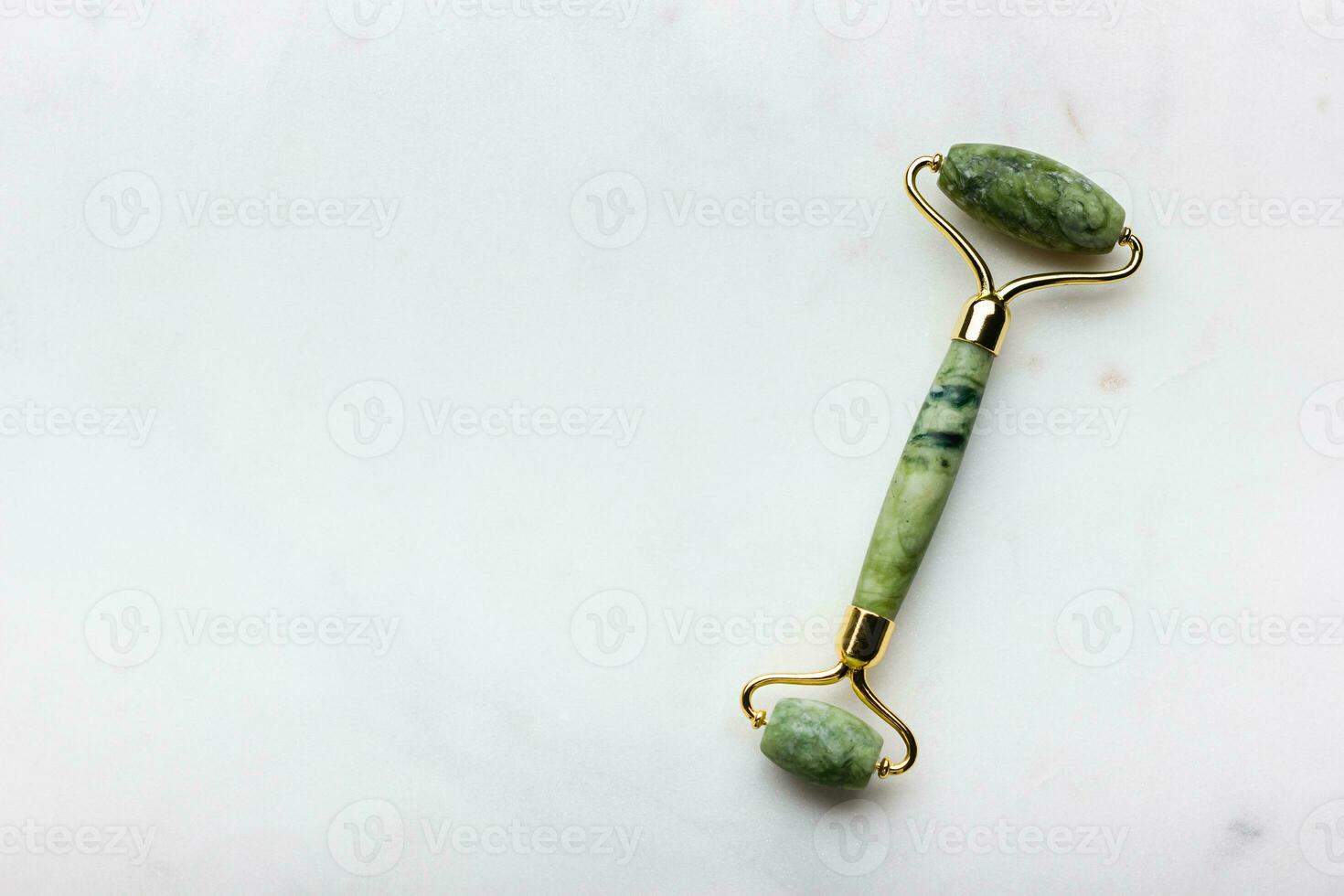 Green jade roller massager for face on white marble. photo