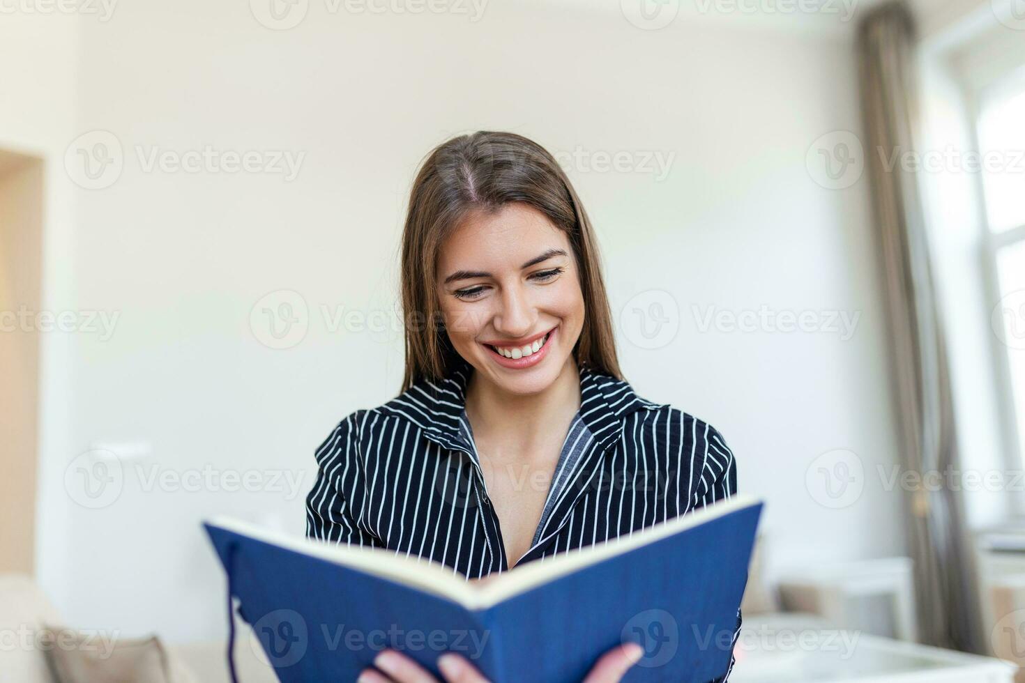 Young beautiful woman holding book, University student studying, learning language. leisure, literature and people concept - smiling woman reading book at home photo