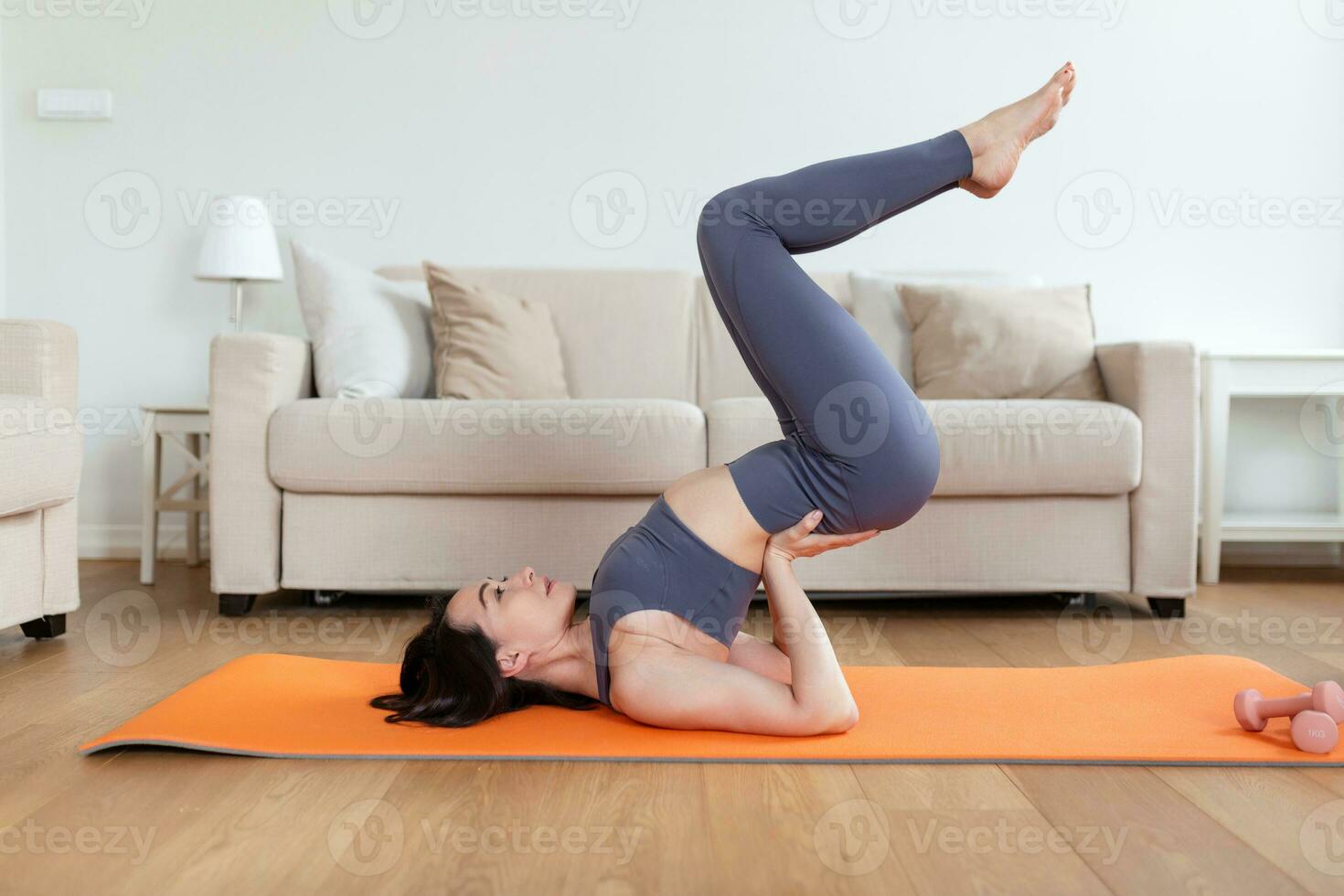 One beautiful Asian woman doing yoga on exercise mat in her living room, lying on upper back and holding her lower back in balance. photo