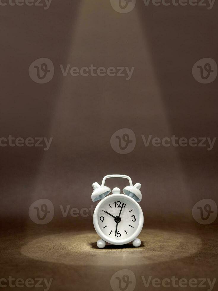 Clock in a beam of light on dark background. Business idea, financial concept and saving money and time. Vertical format photo