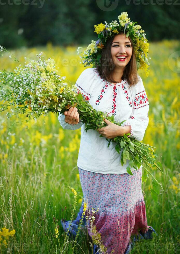 Smiling girl in Ukrainian costume with a wreath on his head in a meadow photo