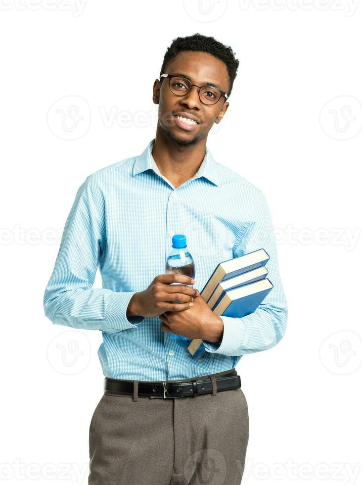 Happy african american college student with books and bottle of water in his hands  standing on white photo
