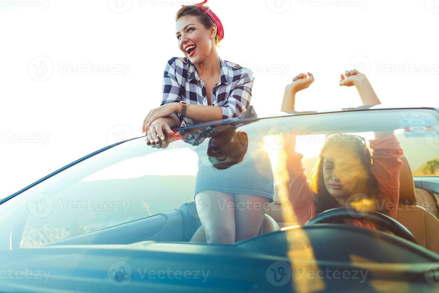 dos joven contento muchachas teniendo divertido en el cabriolé al aire libre foto