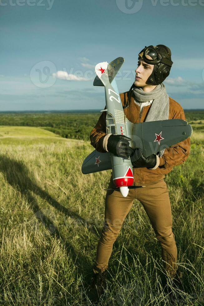 chico en Clásico ropa piloto con un avión modelo al aire libre foto