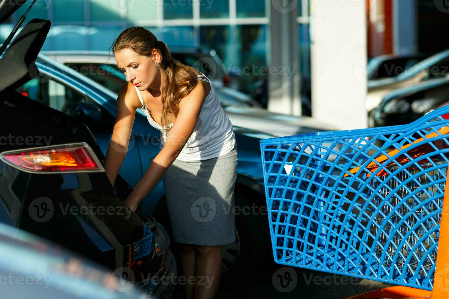 joven mujer turnos el compra desde compras carro en el maletero de un coche en el estacionamiento foto