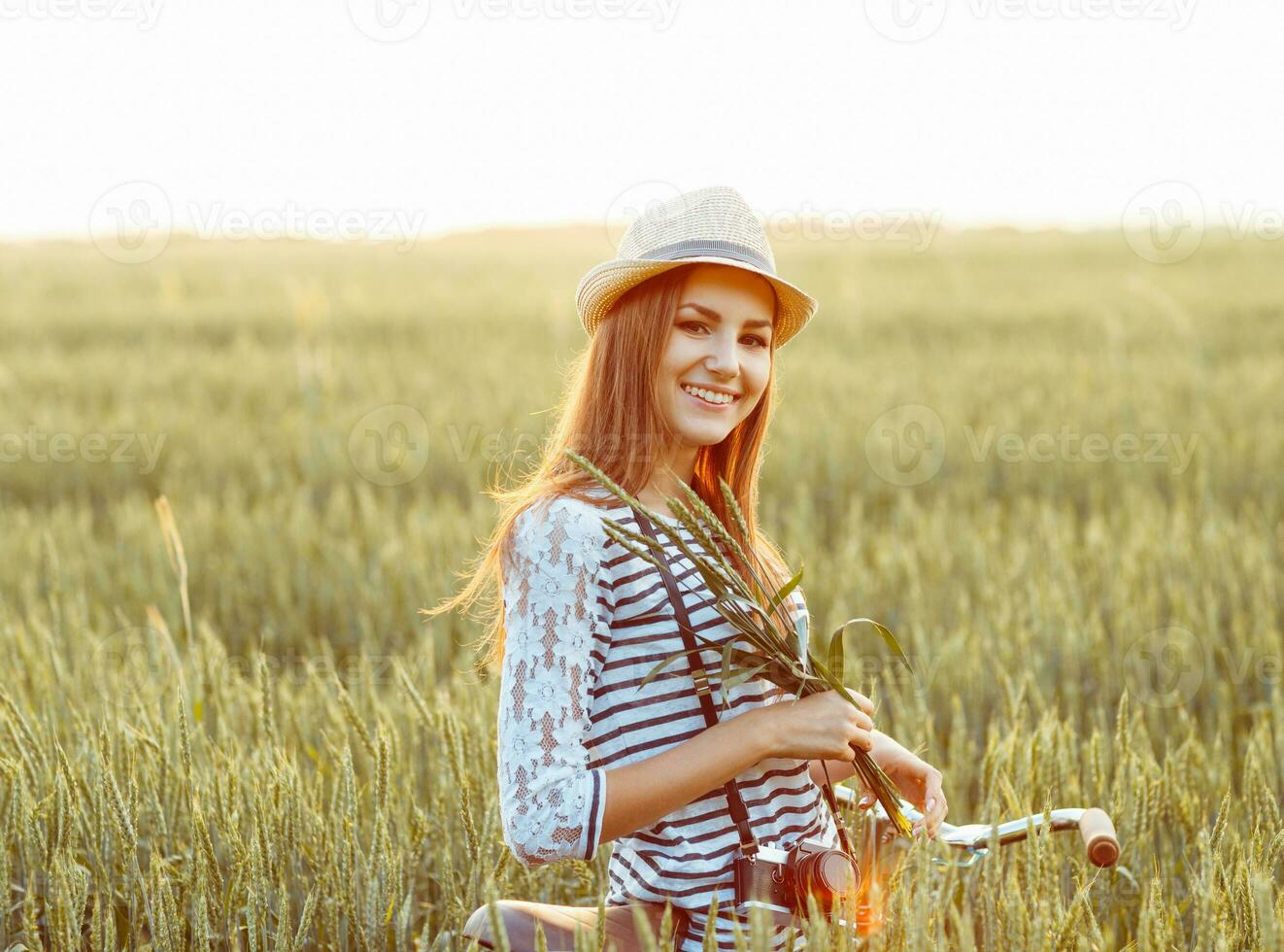 Lovely young woman stands in a field with her bicycle photo