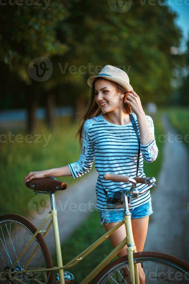 Lovely young woman in a hat with a bicycle in a park photo