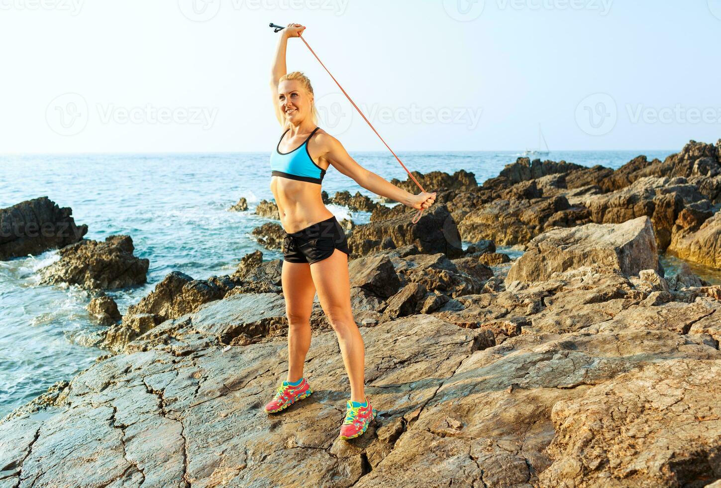 Athlete woman doing sport exercising with the rope on the rocks by the sea photo