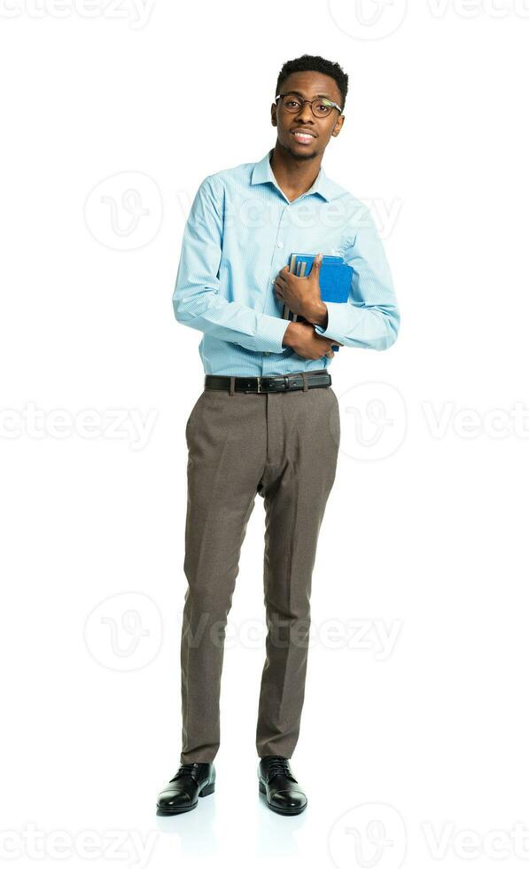 Happy african american college student with books in his hands  standing on white photo