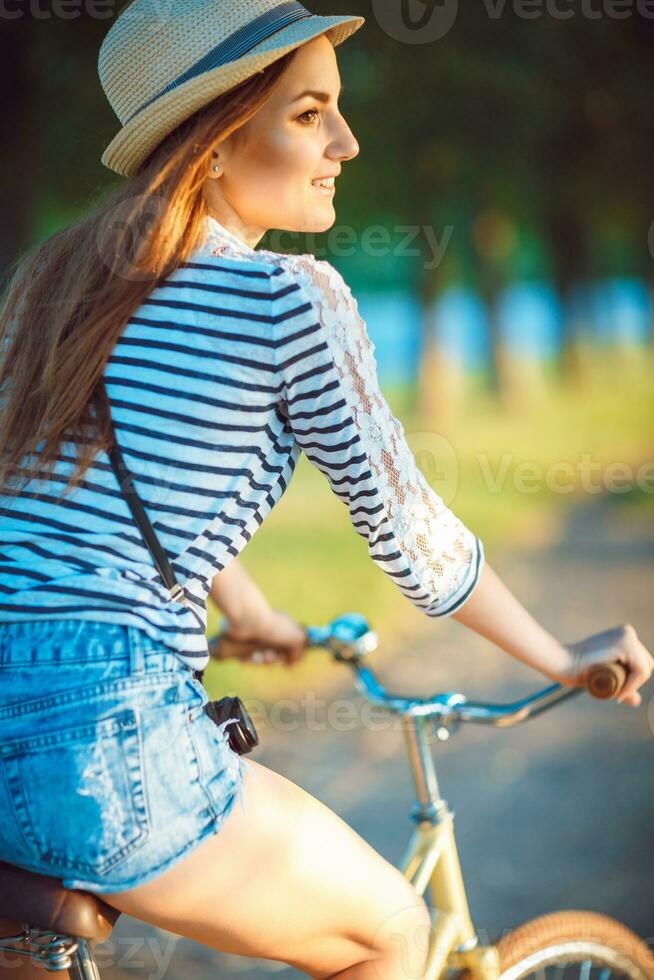 Lovely young woman in a hat riding a bicycle in a park photo