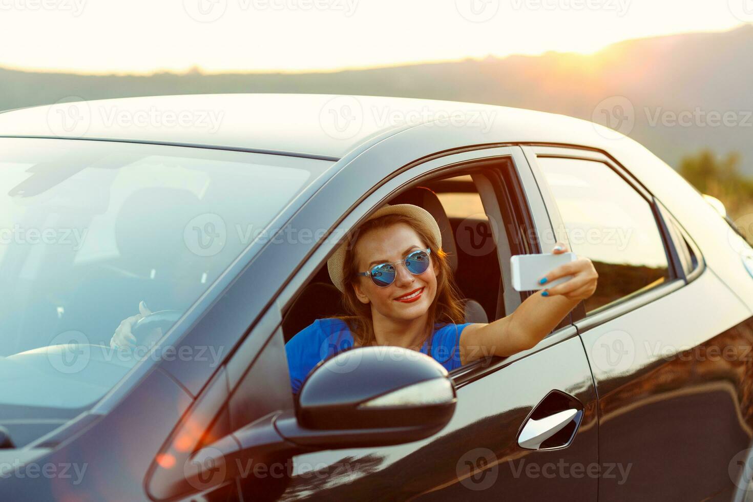 Young happy woman in hat and sunglasses making self portrait sitting in the car photo
