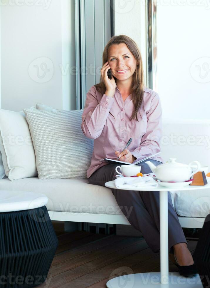 Businesswoman talking on the cellphone and writing in organizer in a coffee house photo