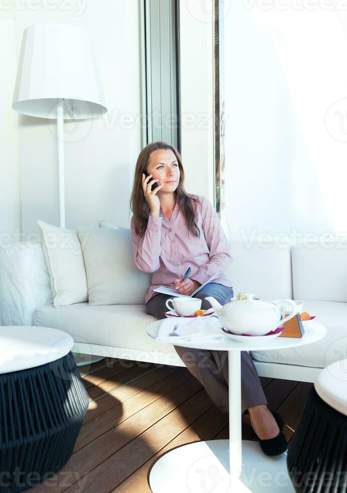Happy businesswoman talking on the phone and writing in organizer in a cafe photo