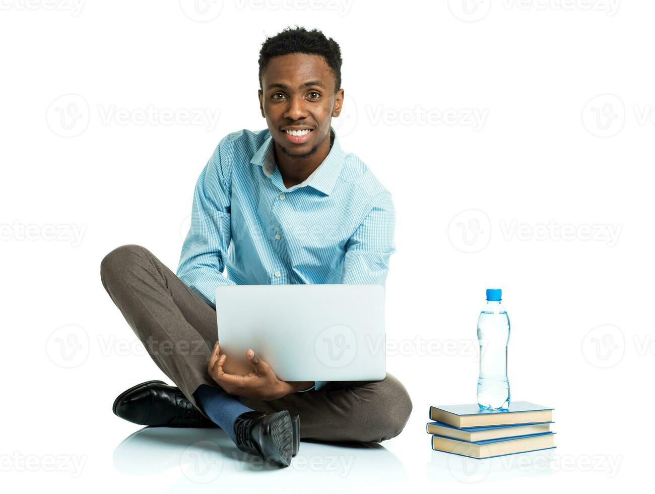 Happy african american college student with laptop, books and bottle of water sitting on white photo