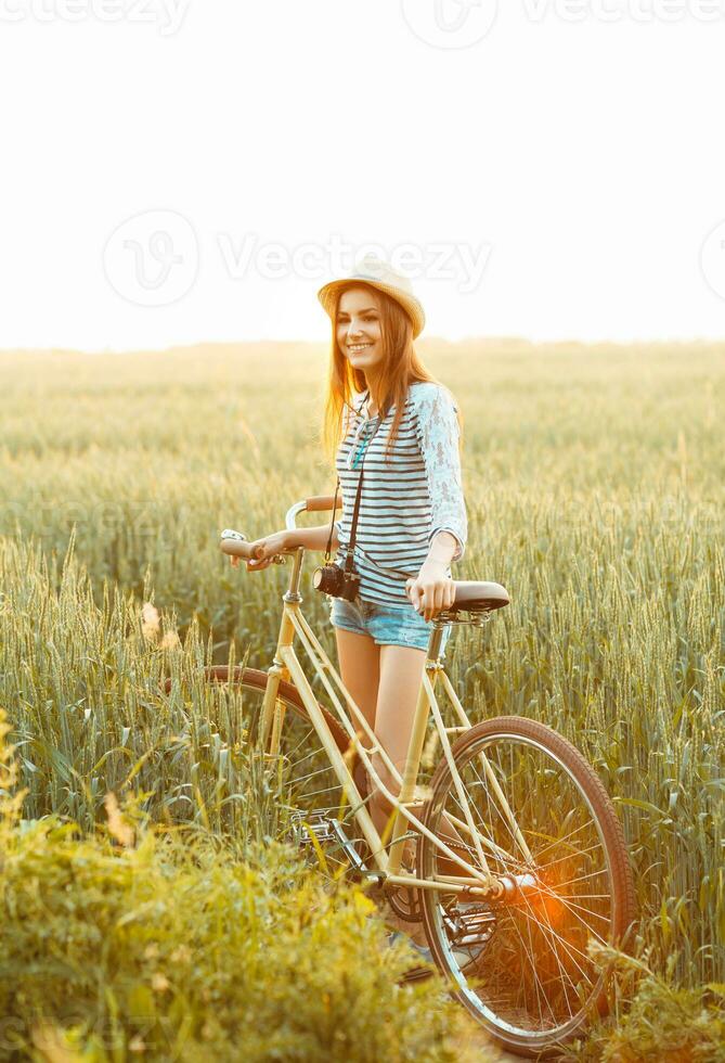 Lovely young woman stands in a field with her bicycle photo