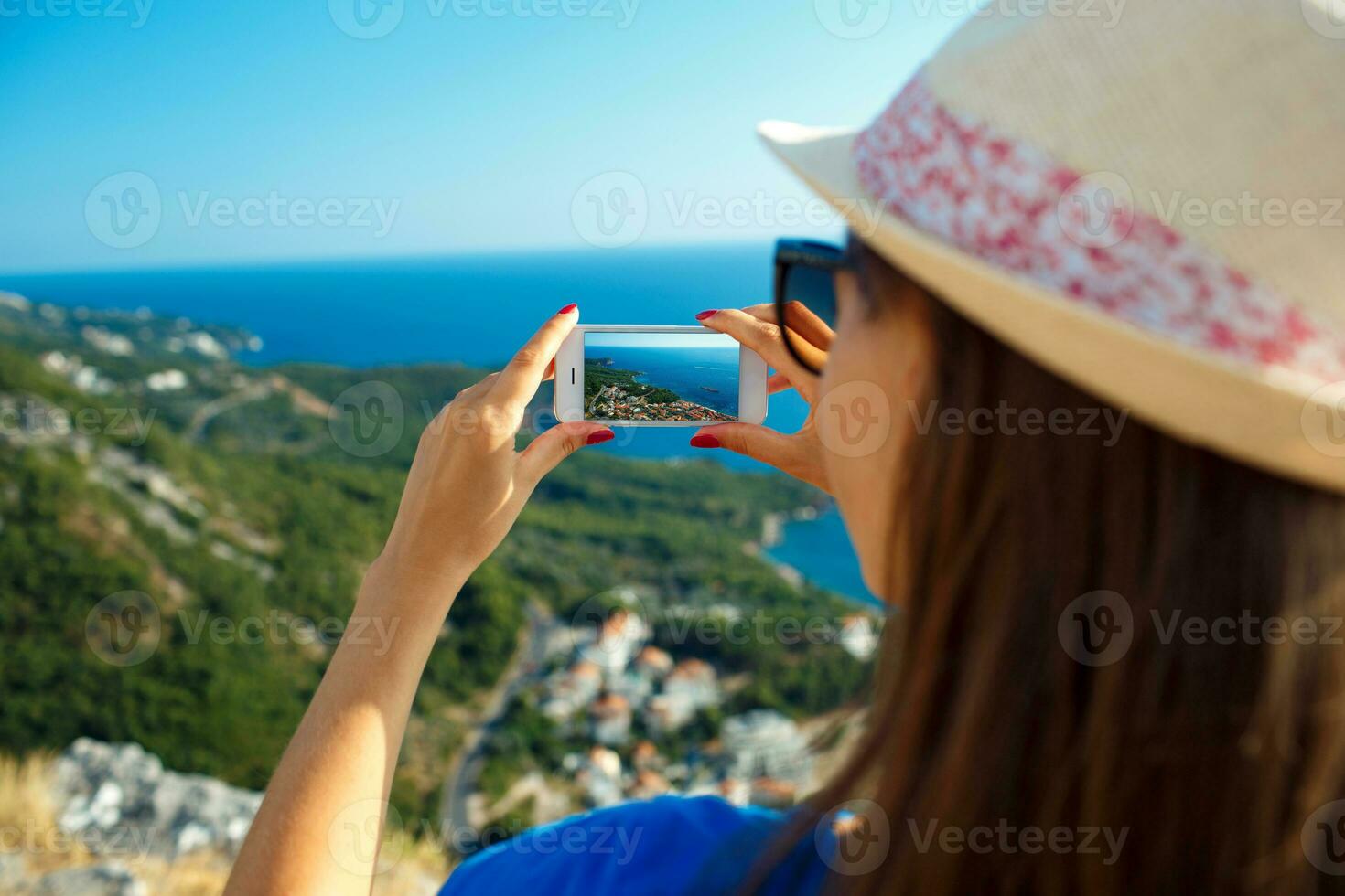 Girl in hat making photos of the Adriatic sea by the smartphone