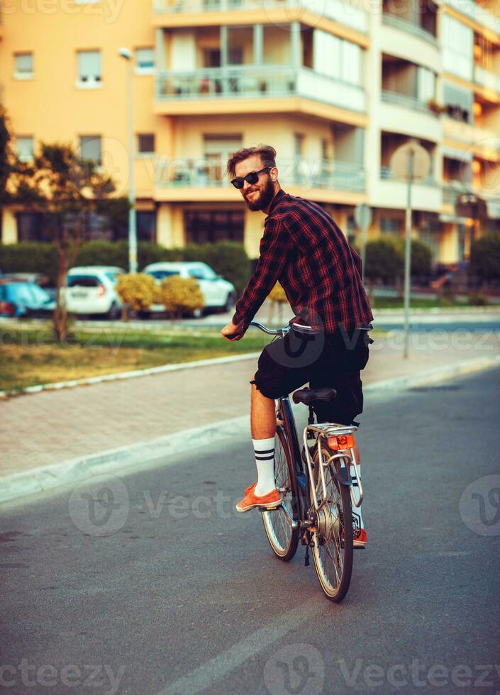 Stylish man in sunglasses riding a bike on city street photo