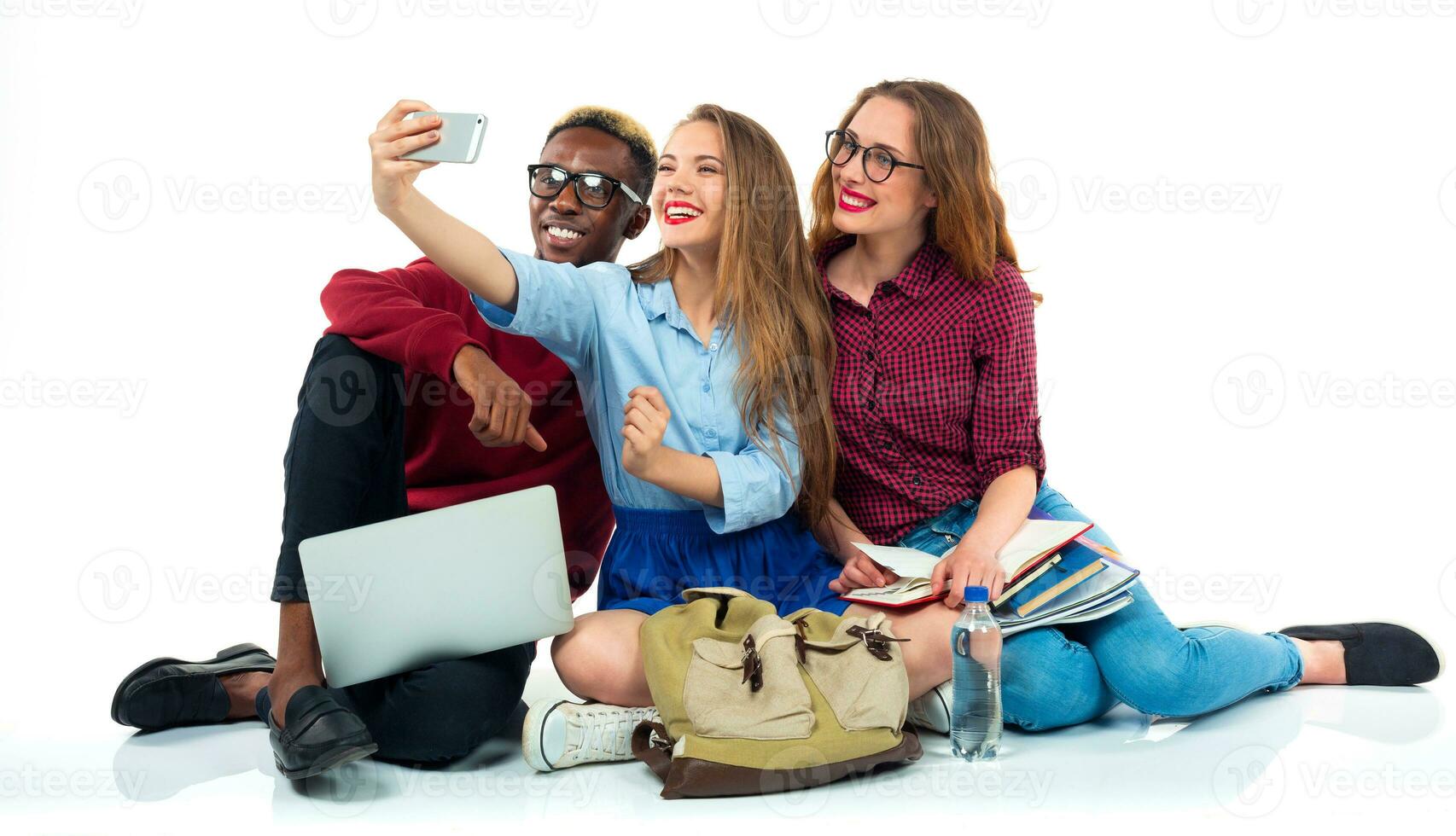 contento estudiantes con libros, computadora portátil, pantalones y hace selfie en blanco antecedentes foto