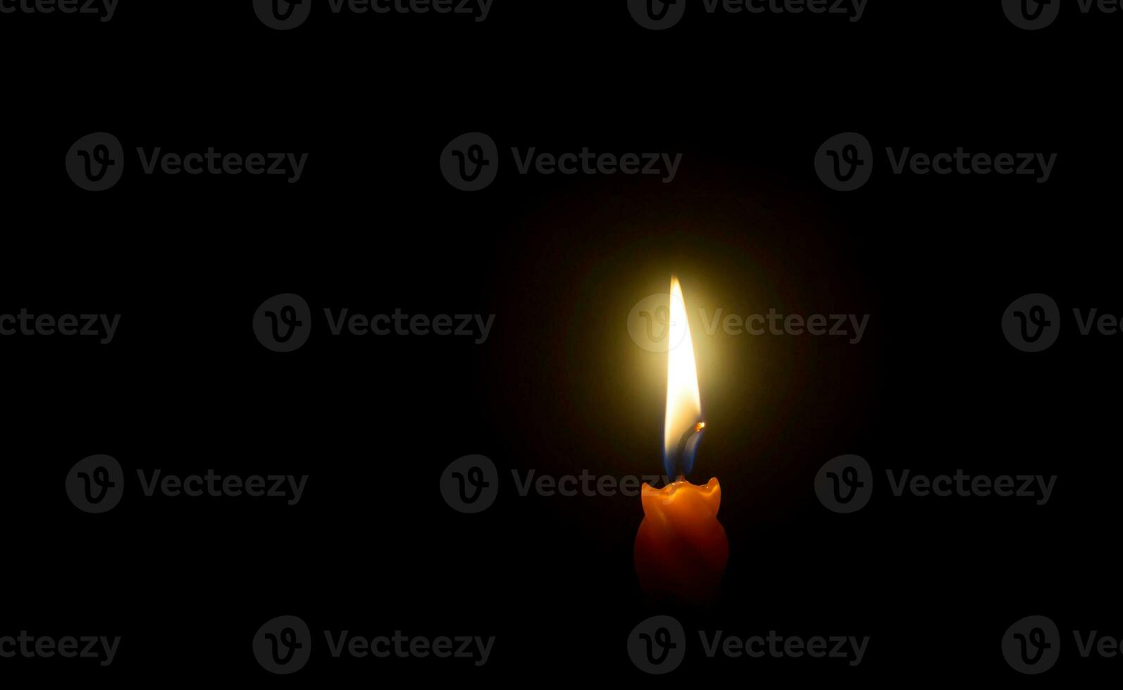 A single burning candle flame or light glowing on spiral orange candle on black or dark background on table in church for Christmas, funeral or memorial service with copy space photo