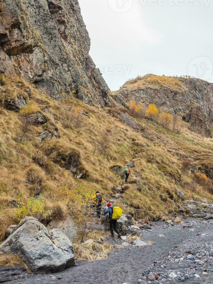 Autumn trekking on footpath alone Caucasus rocks. Group of tourists with backpacks climbs the mountains along the autumn trail. photo
