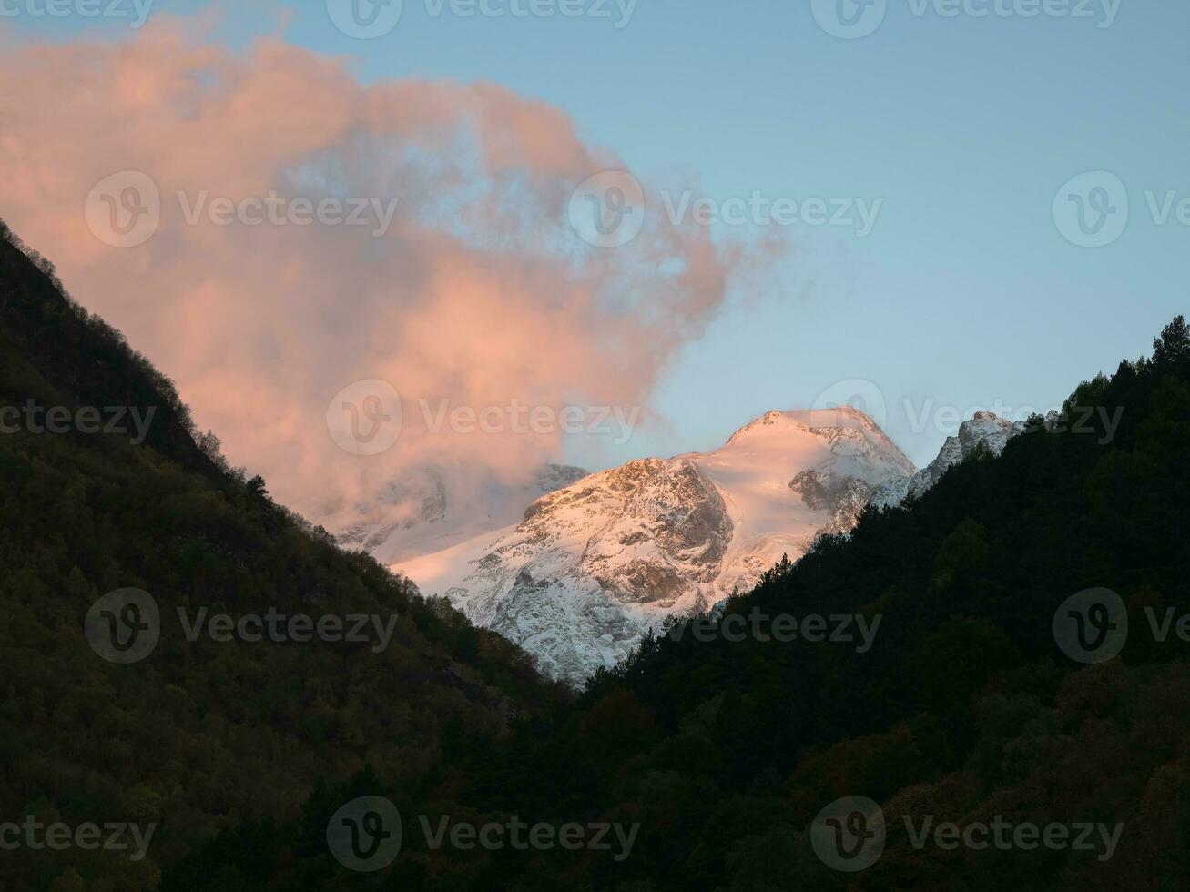 Pink clouds illuminated by the evening sun over the snow mountain. Cumulus pink colored clouds over the winter mountains. photo