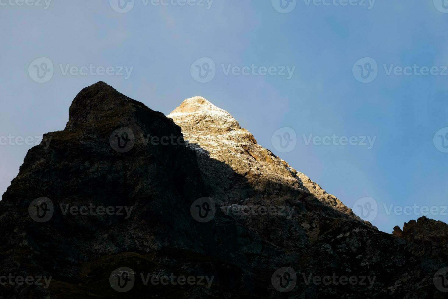 Contrasting mountains at sunset. Evening mountain landscape with snowy rock in golden sunlight. Nature background of rocky mountain walk with sharp rock and blue sky. photo