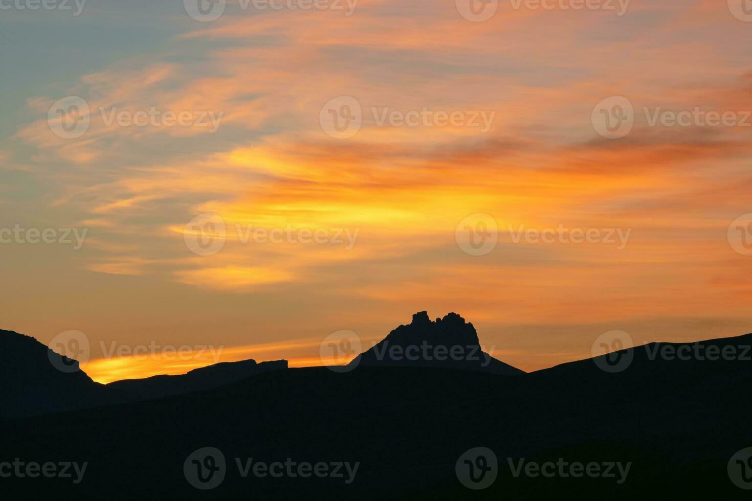 Dark silhouettes of mountains against a bright orange sunset sky. Red sunset over majestic mountains. Sunset in magenta tones. Atmospheric purple landscape with a high-altitude snowy mountain valley. photo