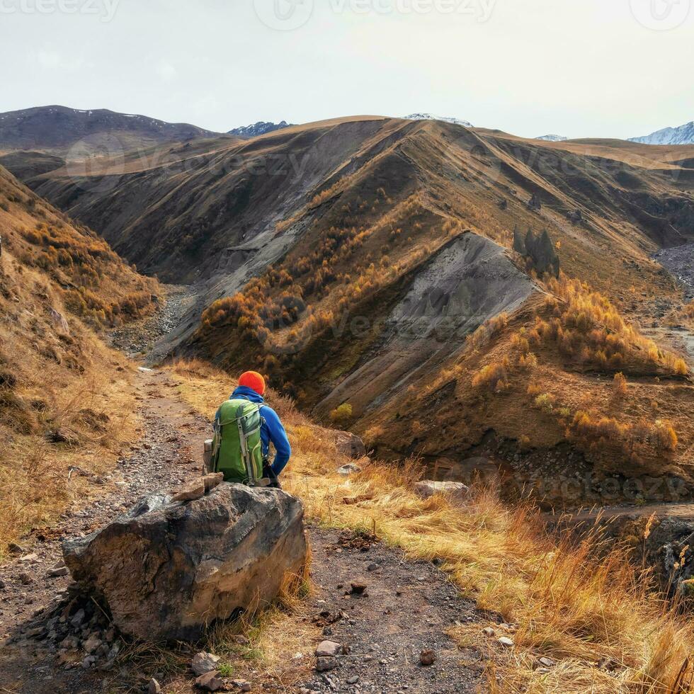 The dreaming hiker sits on a large boulder and happily looks int photo