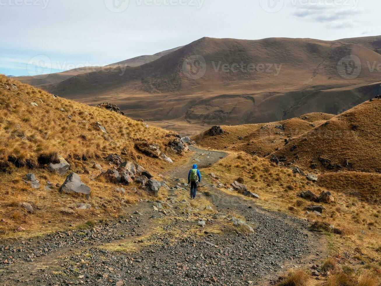 Trekking in the Caucasus mountain. Man with a backpack is climbing heavily on a mountain trail. Adventure solo traveling lifestyle concept, active weekend vacation on the wild nature. photo