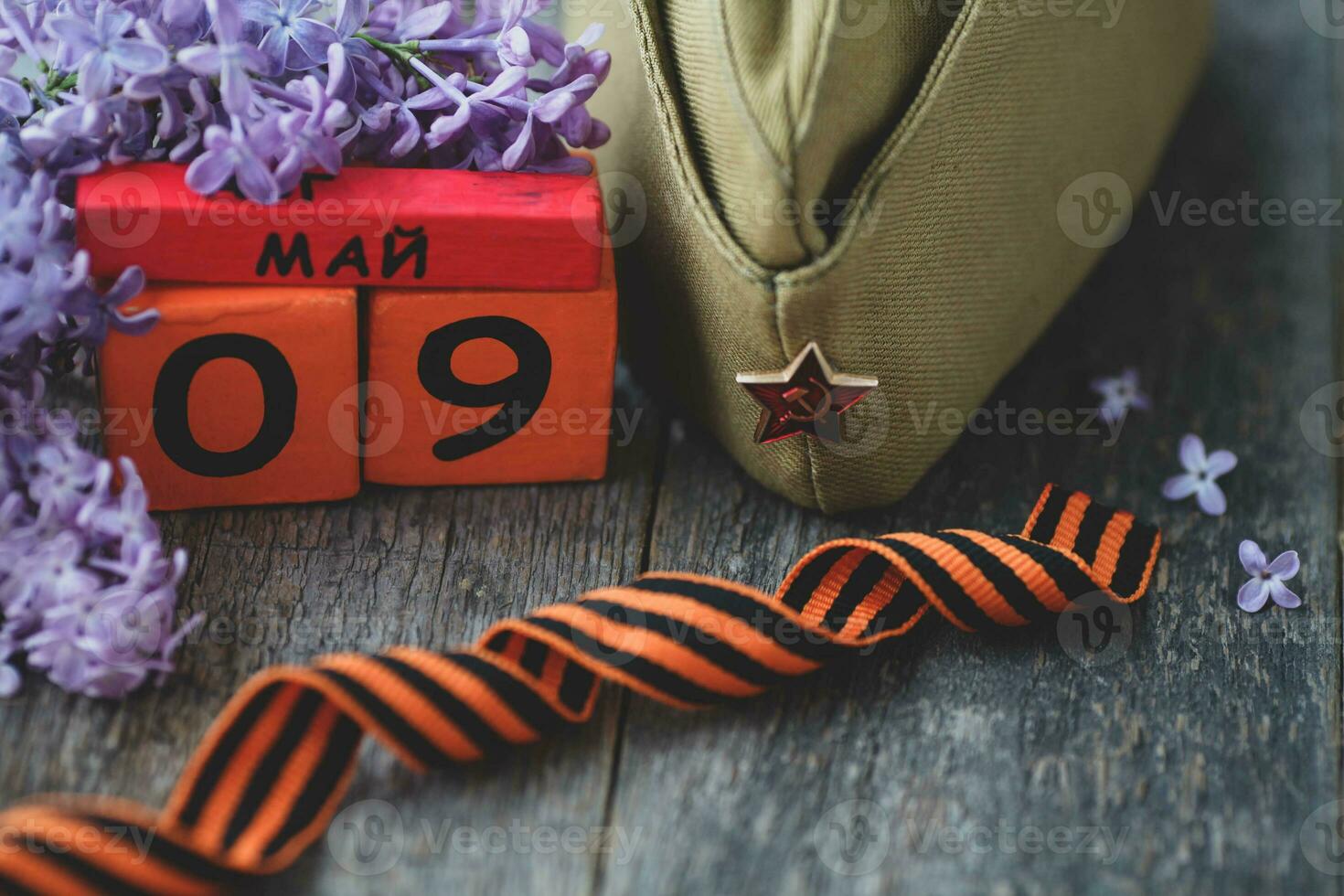 Wooden calendar with Russian text May 9, garrison cap, george ribbon and a bouquet of lilacs on a wooden background. Victory Day. photo