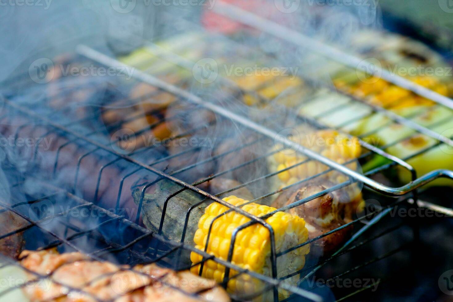 Closeup grilled vegetables on the grill. Corn, mushroom and pepper close-up are cooked on a barbecue, smoke from a fire. photo