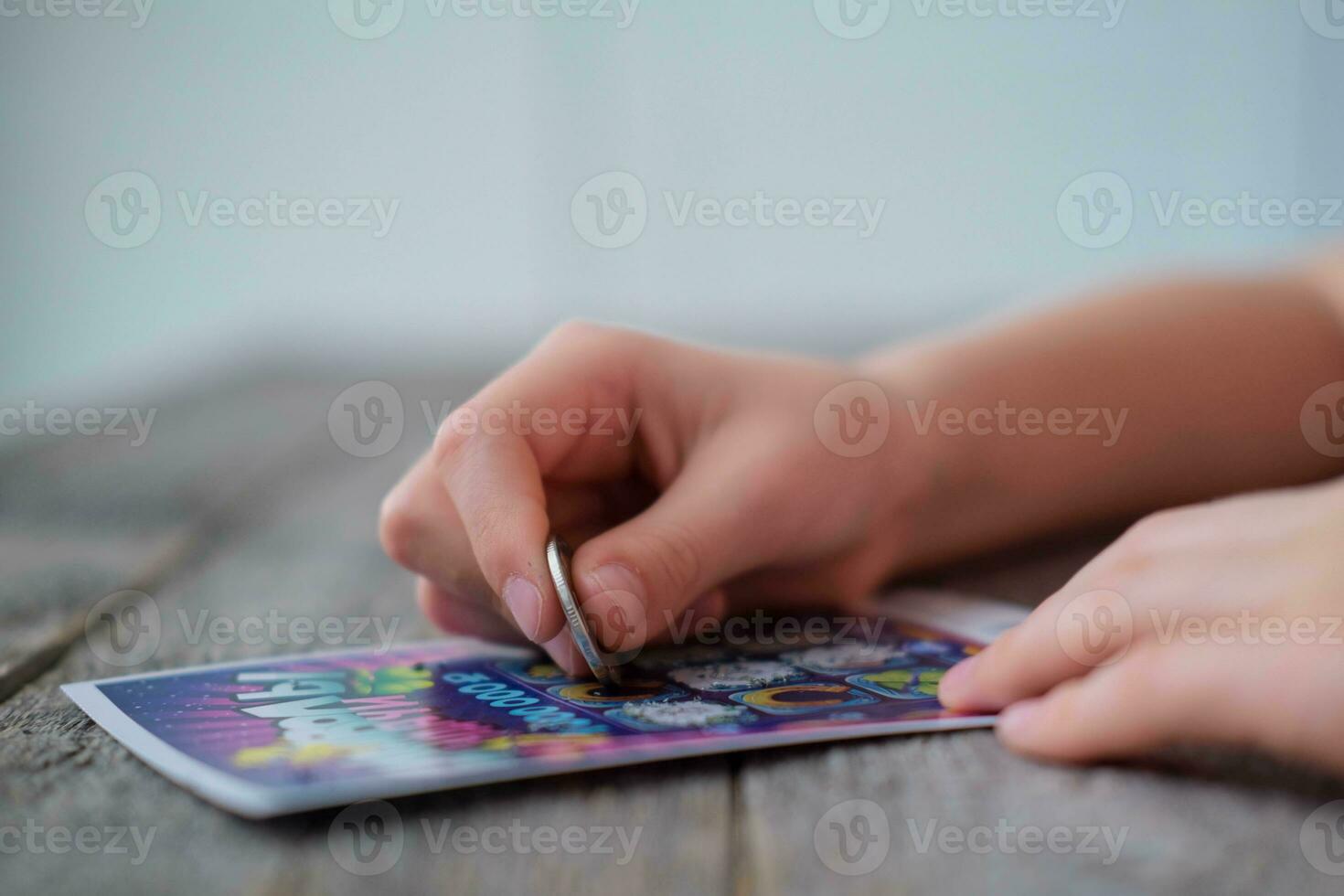 A child is hand erases a protective field in a lottery with a coin on a wooden background. Won. Gambling, addiction. photo